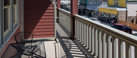 A balcony with a view of a mountain range, featuring a red building, a yellow building, and a green building.
