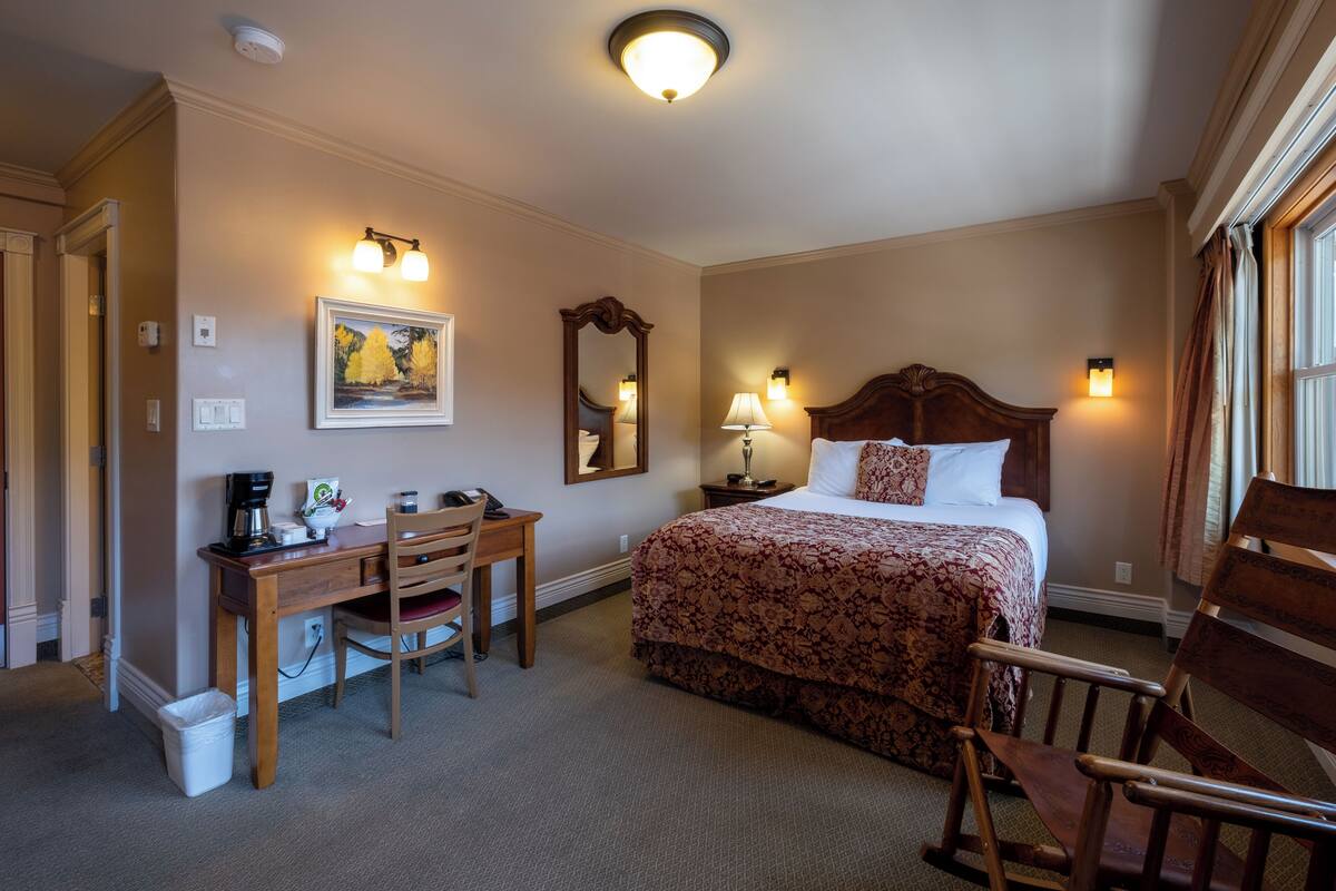 Una habitación de hotel con cama, escritorio, silla y un cuadro en la pared.