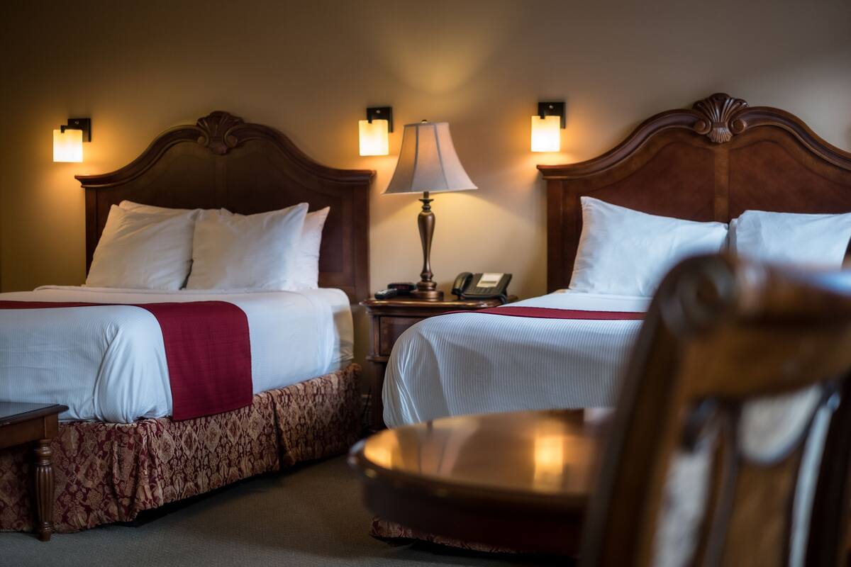 Una habitación de hotel con dos camas, una mesita de noche con lámpara y una silla.