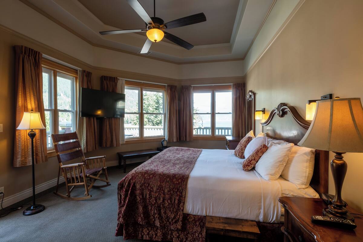 Habitación de hotel con una cama, ventilador de techo, televisión y ventana con cortinas.