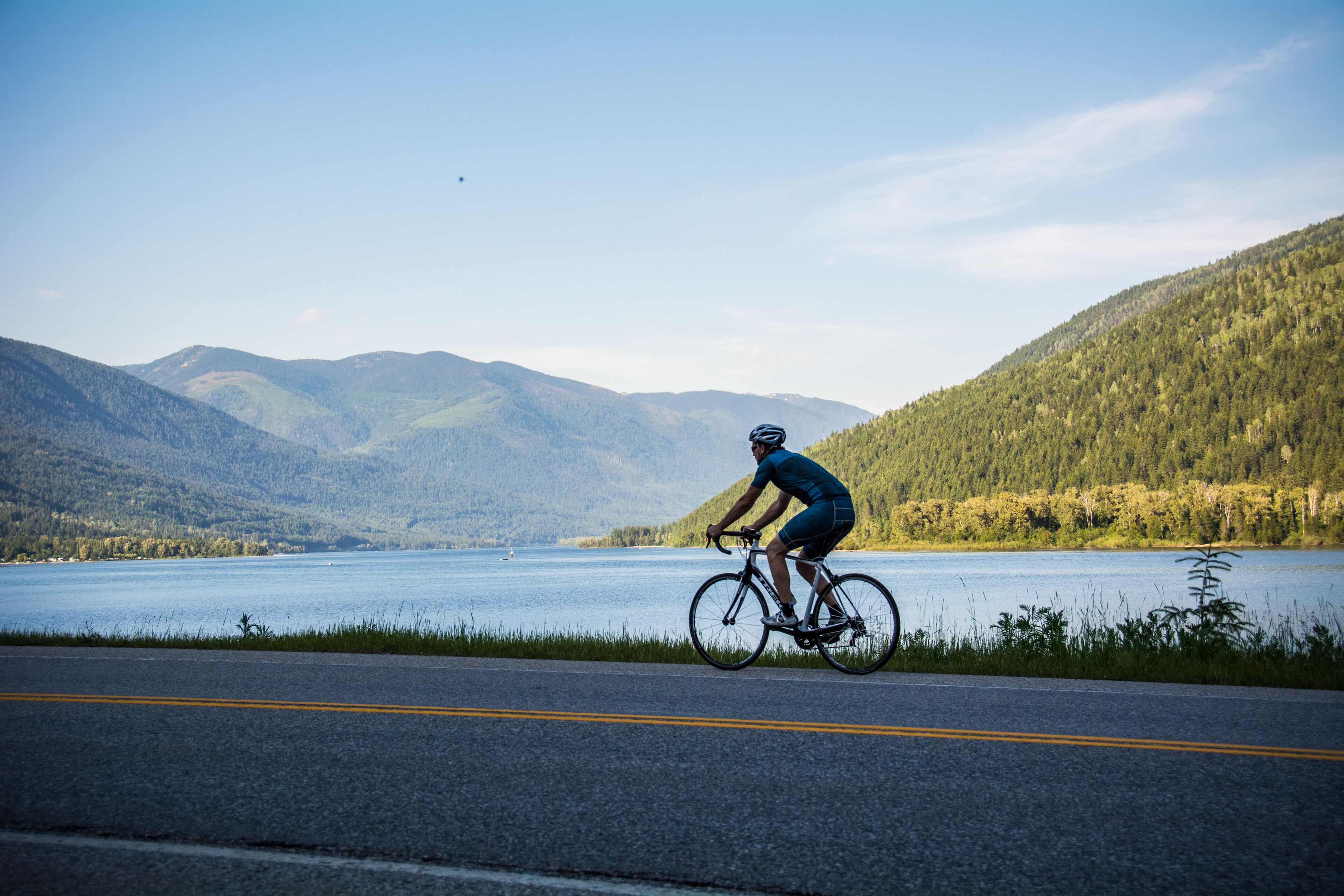 A cyclist on a road with a lake and mountains in the background.