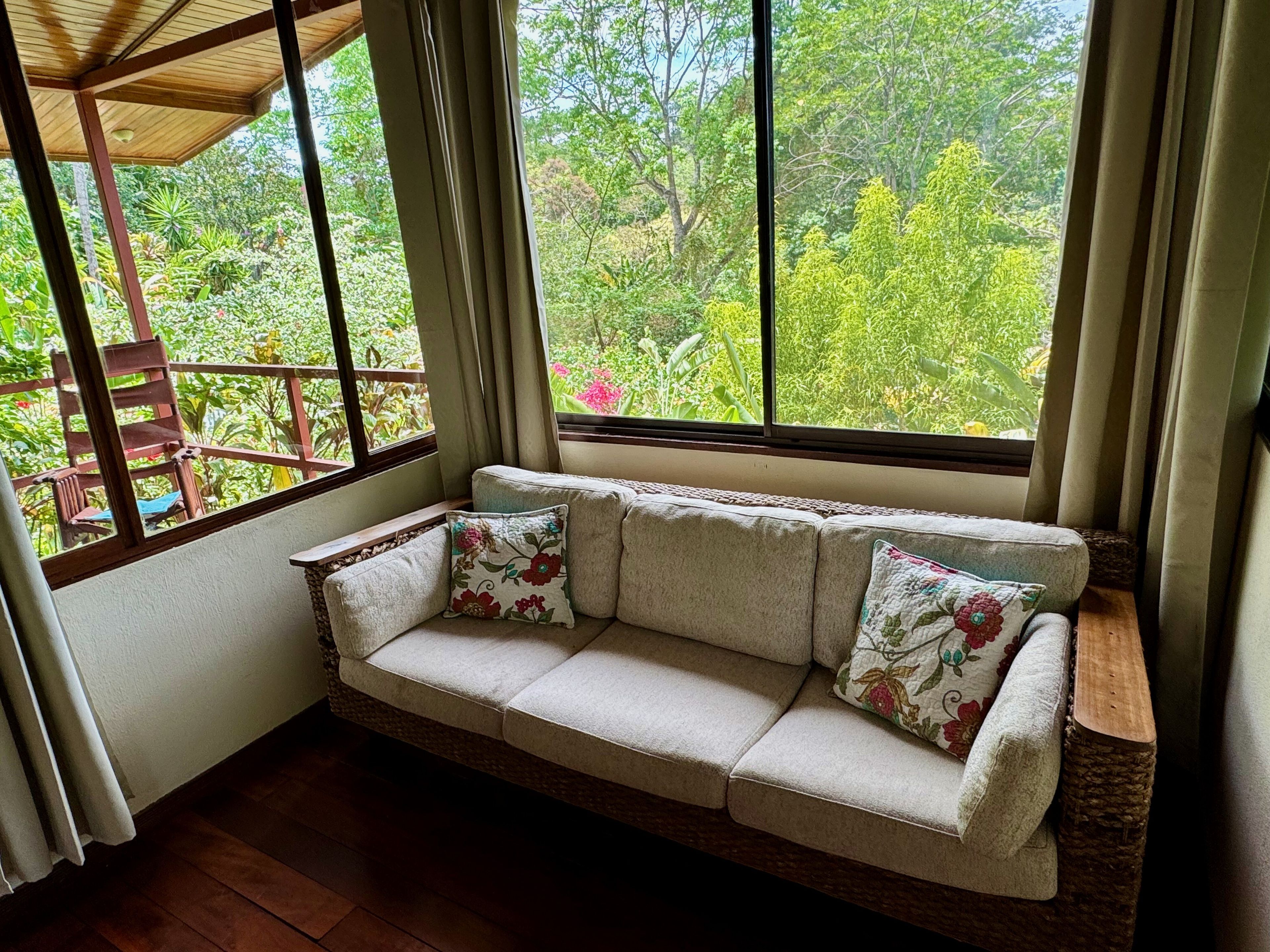 Una habitación con un banco de madera, un banco acolchado con cojines estampados, y vistas a la vegetación a través de amplias ventanas.