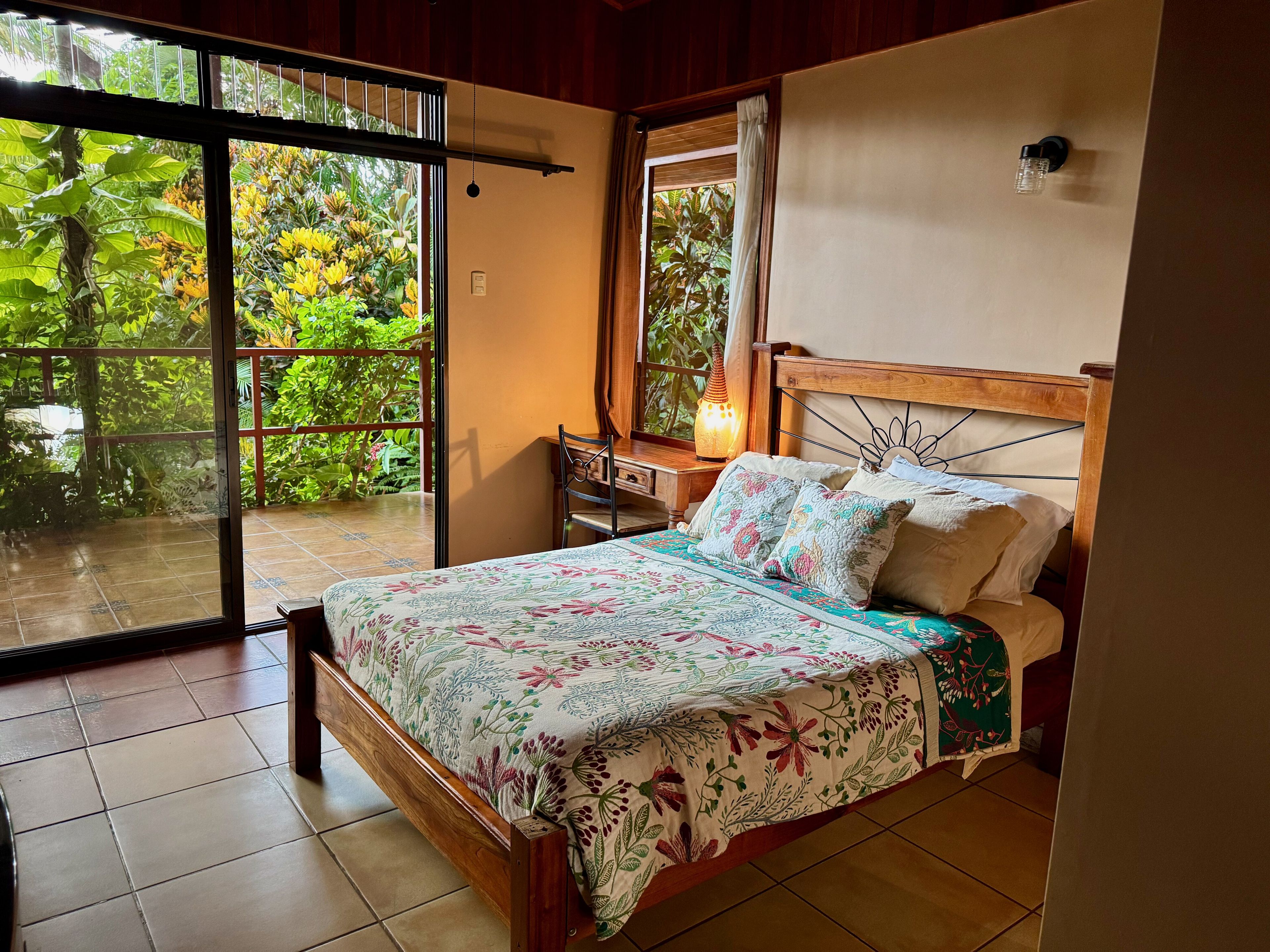 A bedroom with a bed, a desk, and a view of greenery through a sliding door.
