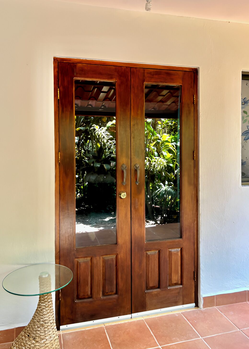 A wooden double door with glass panels, a glass table, and a tiled floor.