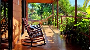 A covered outdoor seating area with a wooden bench, a hammock, and a view of lush greenery. - Eden Atenas (Mercedes)
