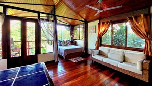 A room with a bed, a sofa, a ceiling fan, and large windows. - Eden Atenas (Mercedes)