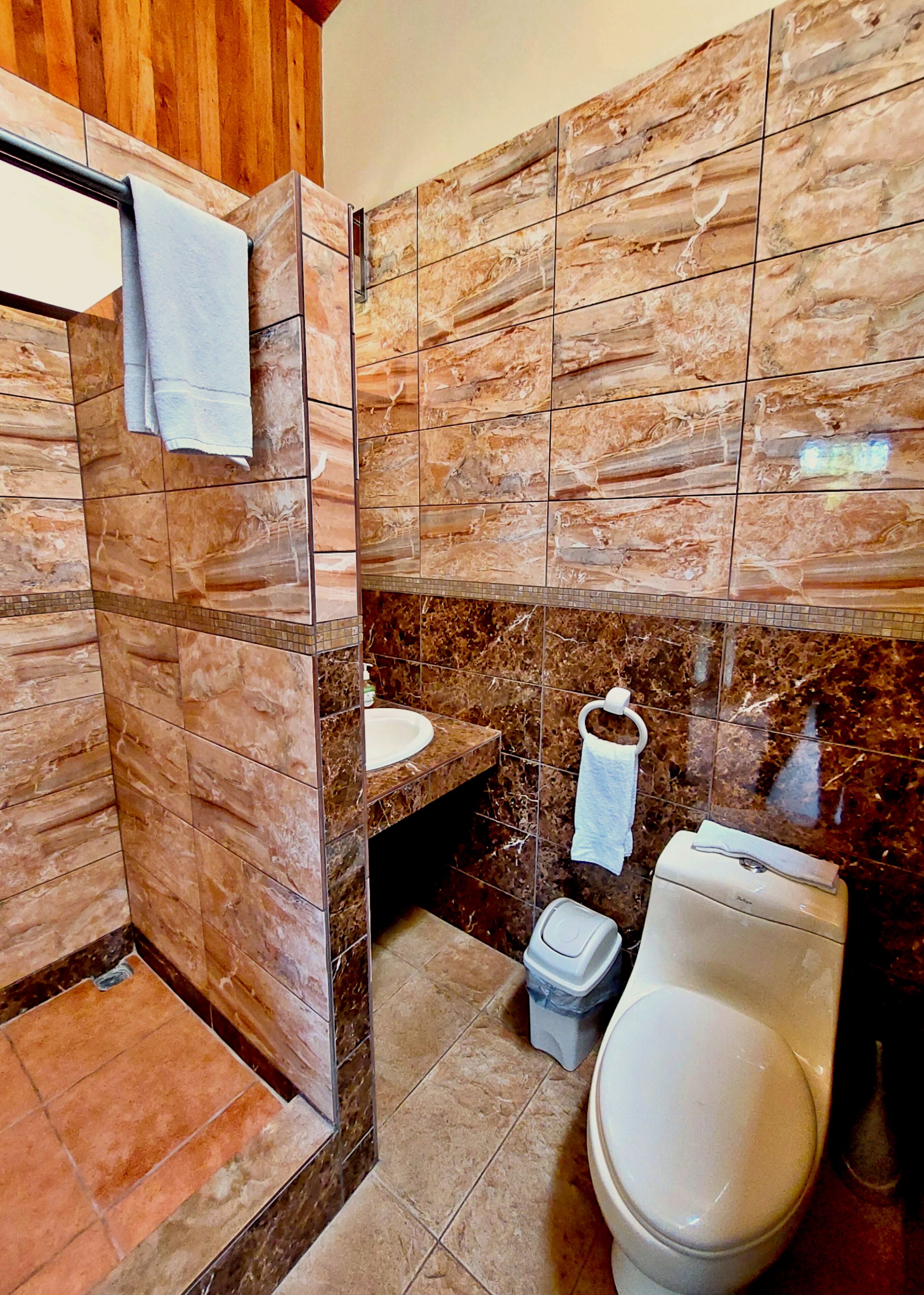 A bathroom with a wooden shower enclosure, a sink, a toilet, and a towel rack.