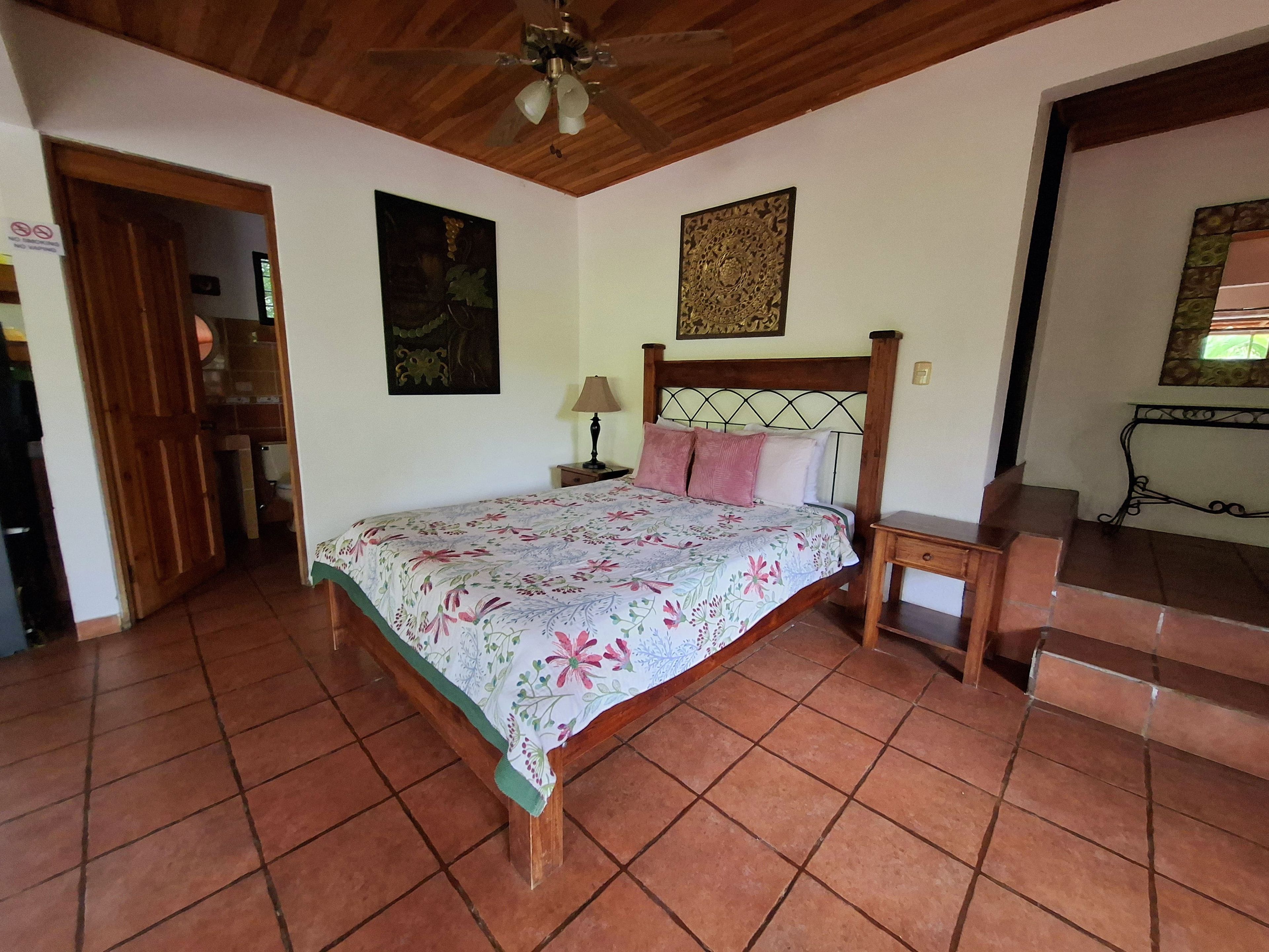 A bedroom with a bed, a nightstand, a wooden headboard, a ceiling fan, a door, and a staircase.