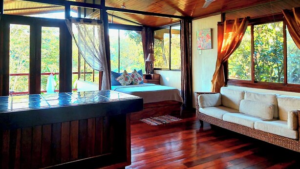 A room with a wooden ceiling, a bed with pillows, a sofa, and a wooden table. - Eden Atenas (Mercedes)