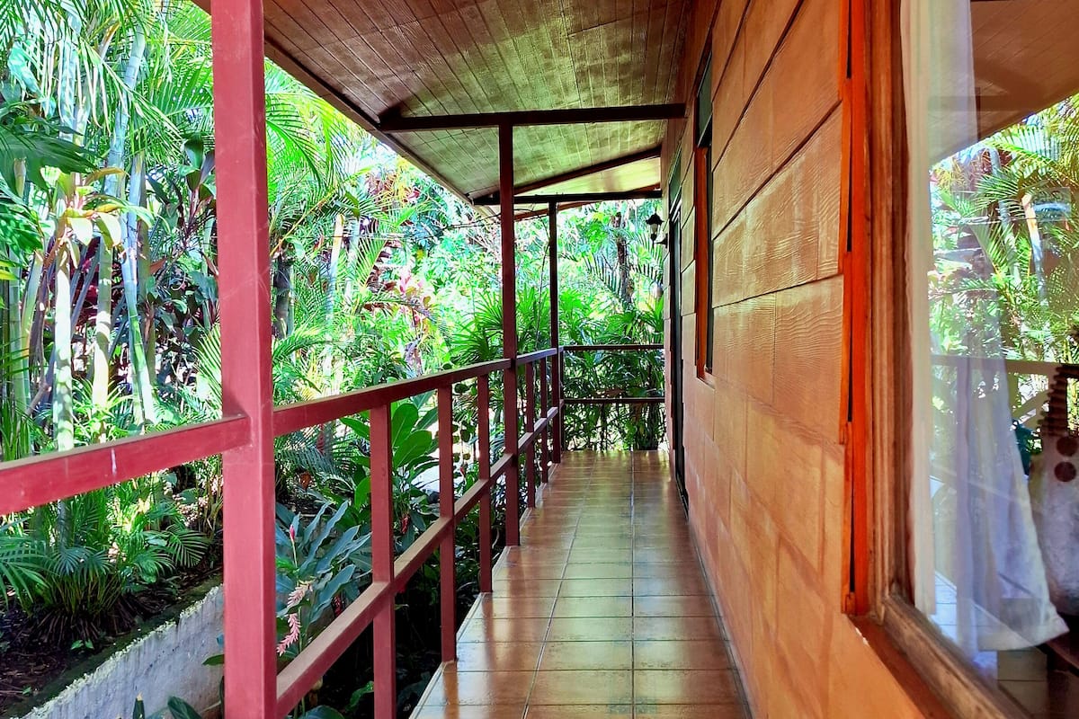A covered corridor with tiled flooring, wooden walls, and a red railing.