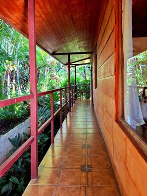 A covered corridor with tiled flooring, wooden walls, and a red railing. - Eden Atenas (Mercedes)