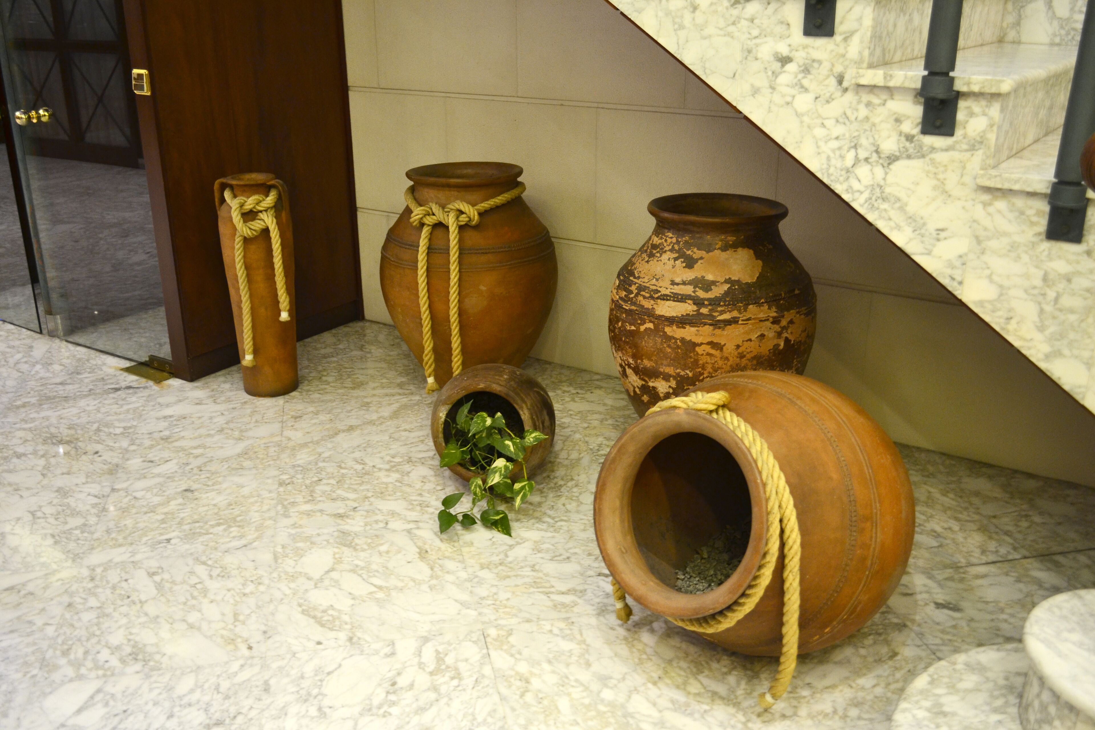 Macetas de terracota con cuerdas enrolladas, sobre un suelo de mármol cerca de una escalera.
