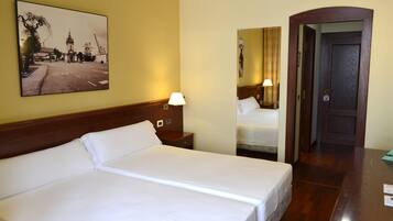 Habitación de hotel con una cama grande, una mesita de noche con lámpara, un espejo y una puerta que da a otra habitación.