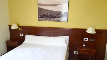Habitación de hotel con una cama, dos mesitas de noche, una lámpara de pared y un cuadro con un paisaje.