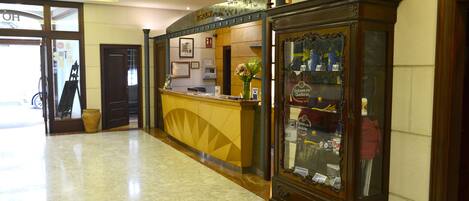 A hotel reception area with a marble floor, a reception desk, and a large wooden display cabinet.
