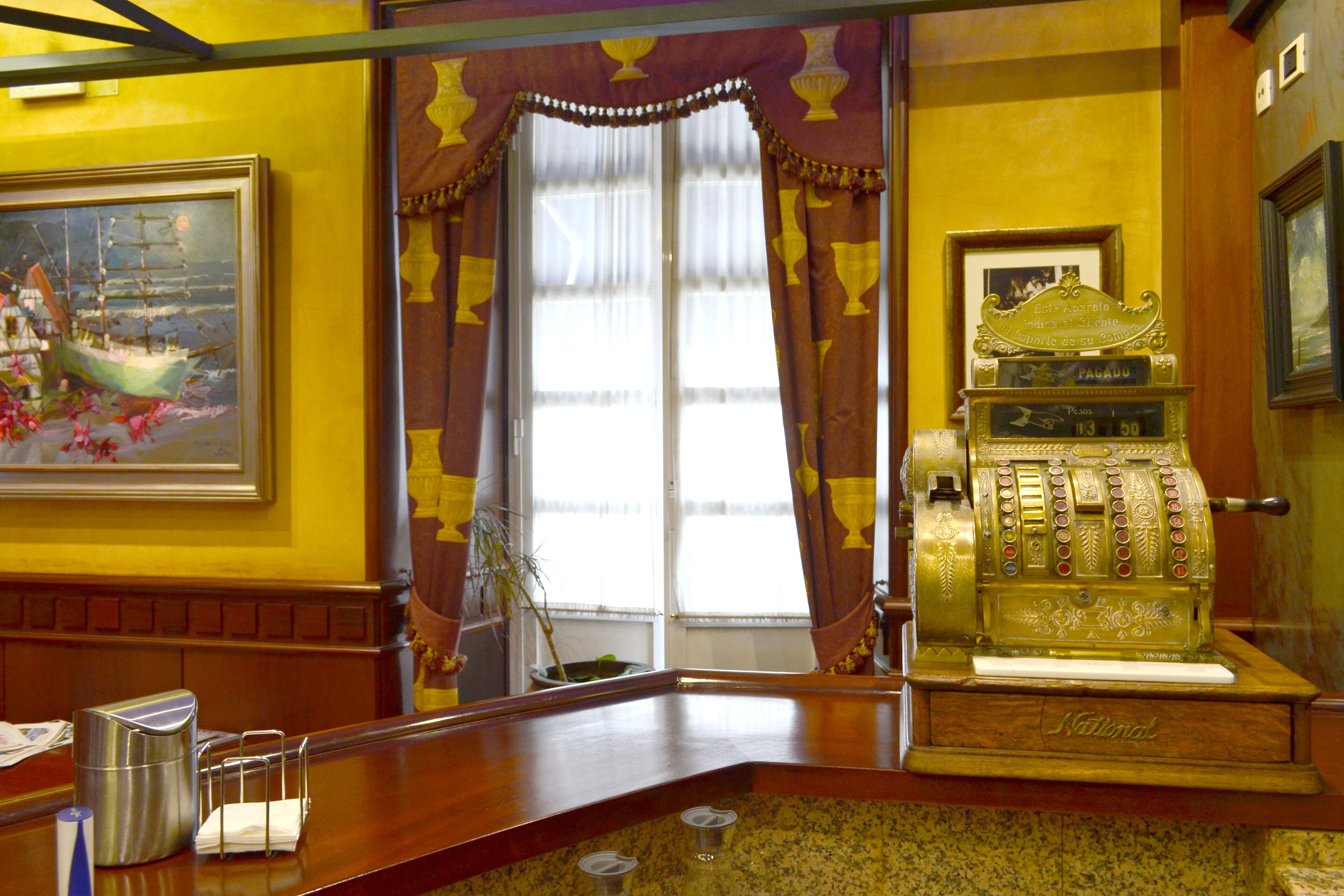A vintage slot machine, a framed painting of a ship, and a window with curtains.