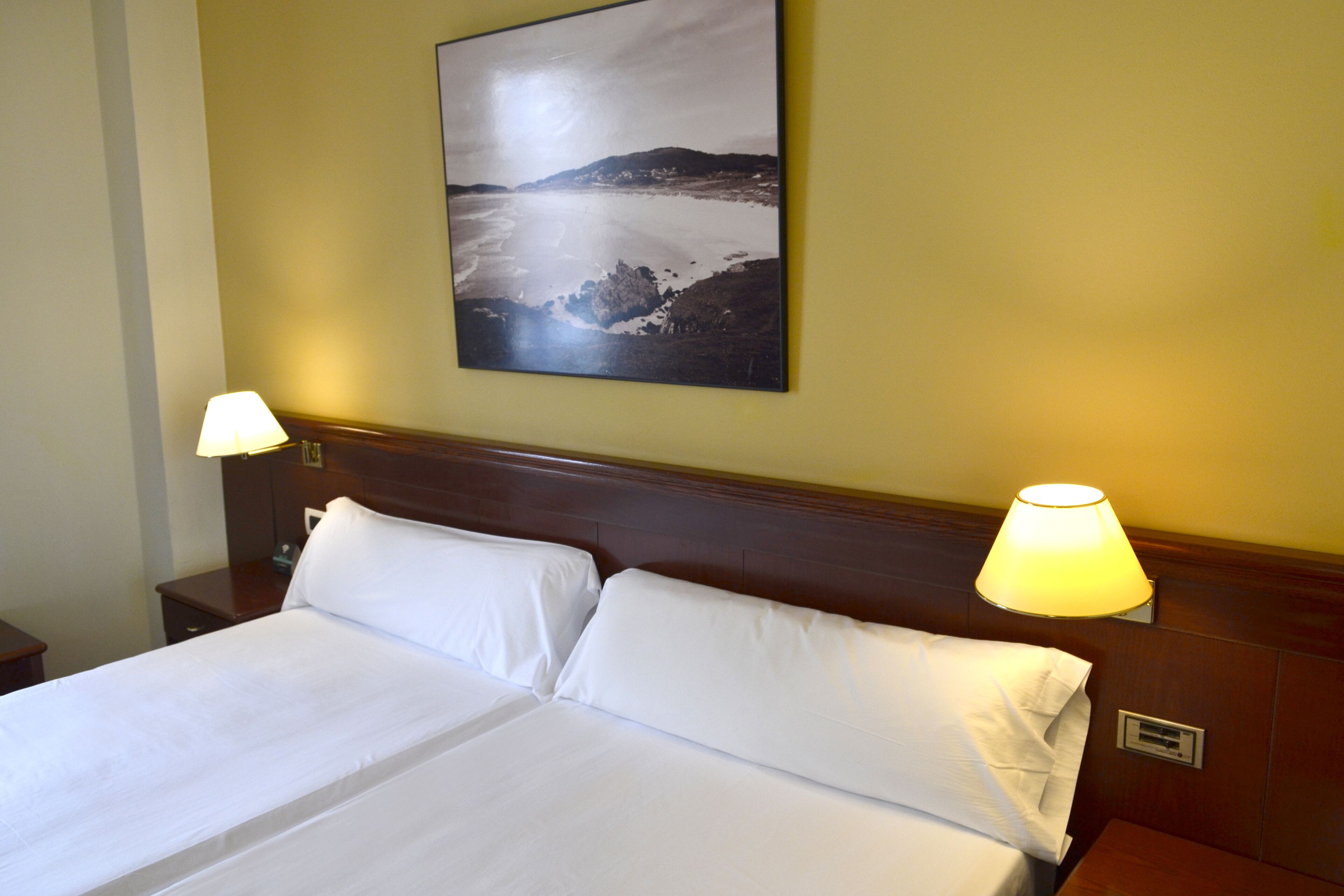 A hotel room with a large bed, two bedside lamps, and a framed landscape picture on the wall.