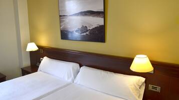 Una habitación de hotel con una cama grande, dos lámparas de noche y un cuadro de paisaje en la pared.