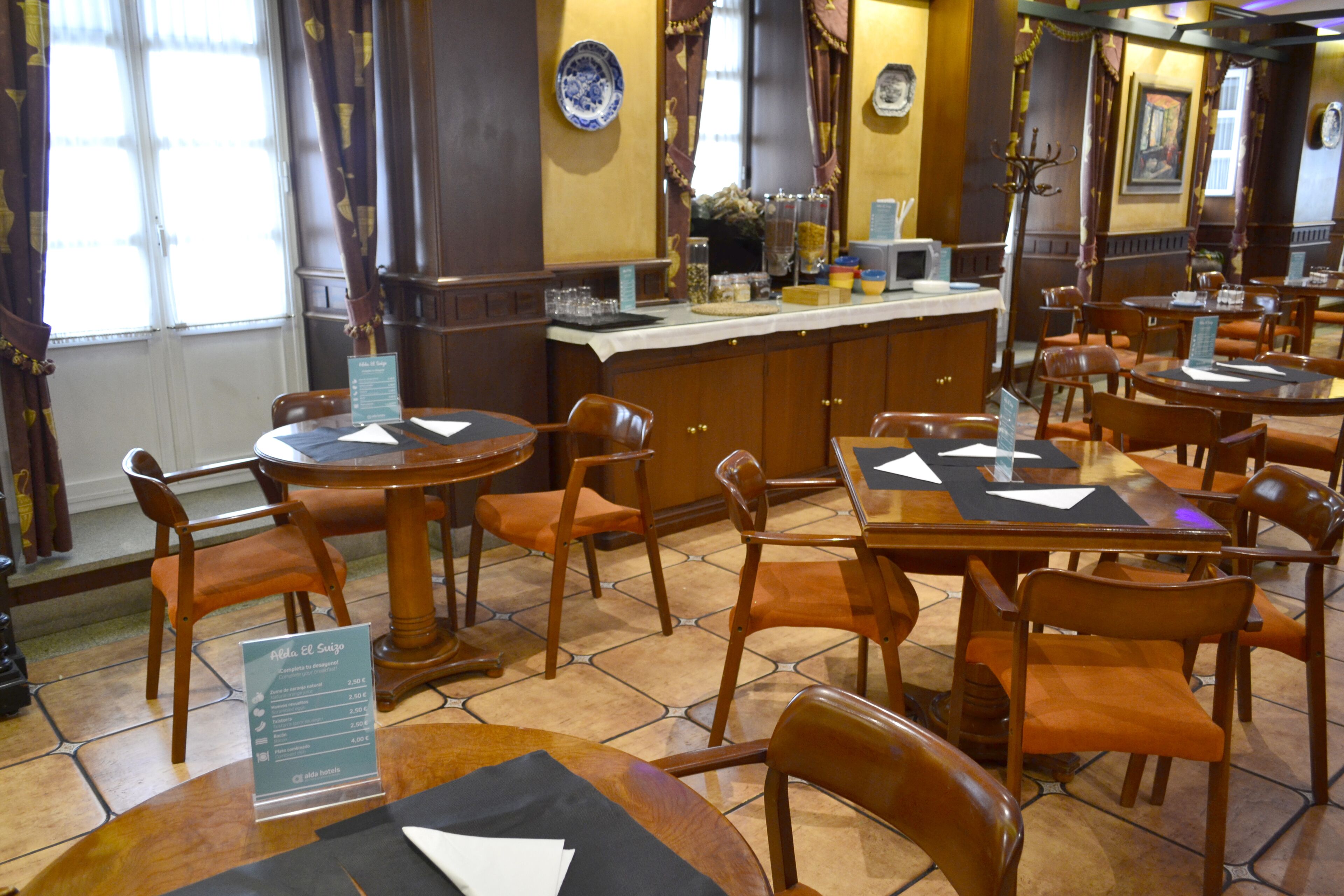 Un interior de restaurante con mesas y sillas de madera, una zona de bar y un atril para el menú.