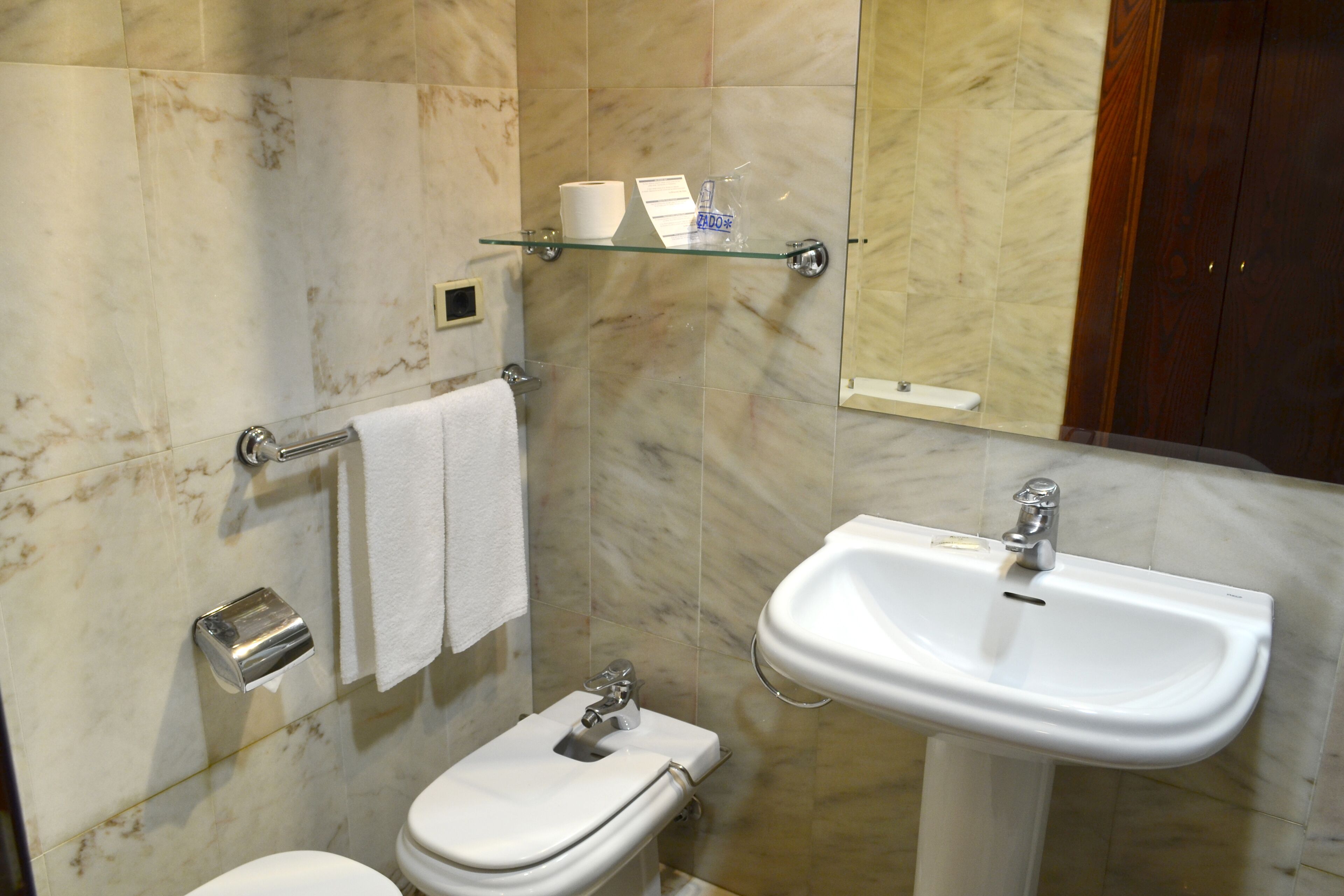 A bathroom with a toilet, a sink, a glass shelf with toiletries, and a towel rack.