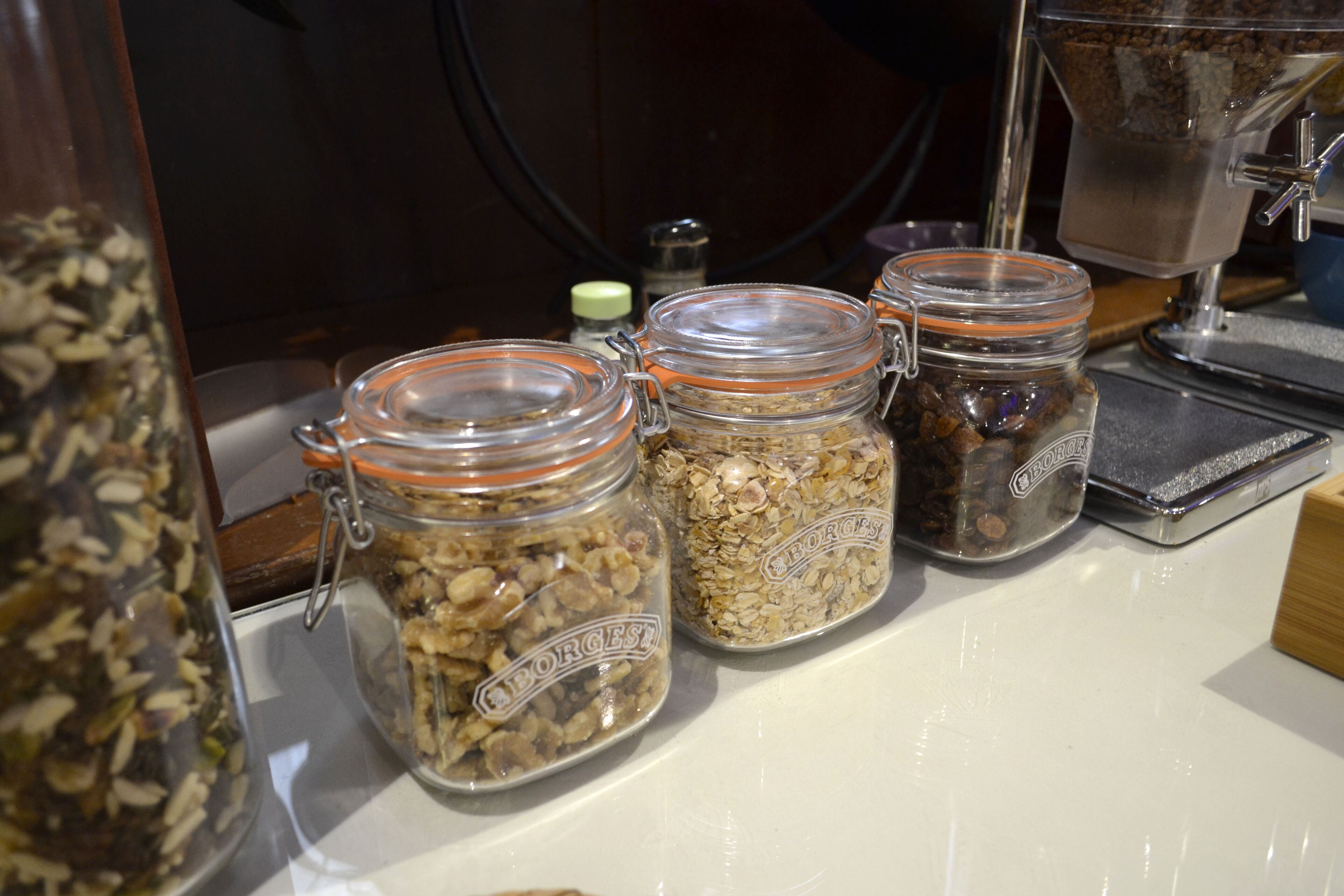 Tres frascos de vidrio con tapas metálicas que contienen diferentes tipos de granos o semillas sobre una encimera.