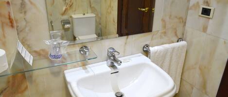 A bathroom with a white sink, a glass soap dispenser, a mirror, and a towel hanging on the wall.