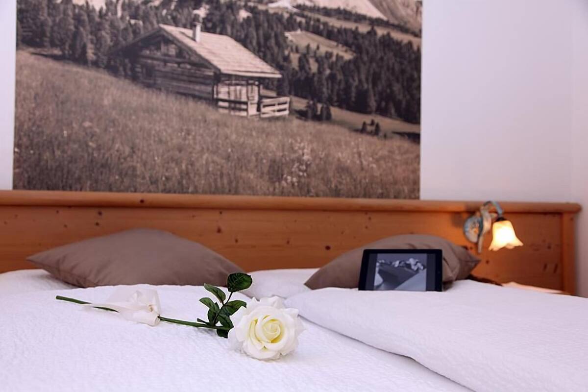 Un llit amb una rosa blanca, una tauleta tàctil i un quadre a la capçalera de fusta.