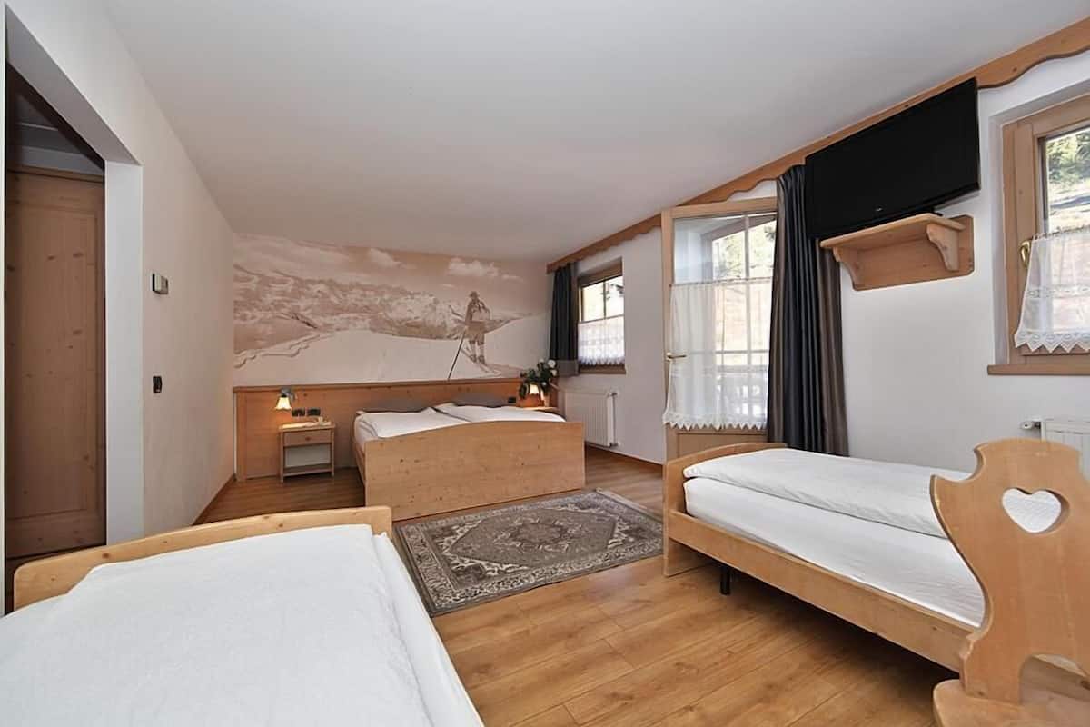 Una habitació amb dos llits de fusta, un mural gran a la paret, un televisor muntat a la pared i una finestra amb cortines.
