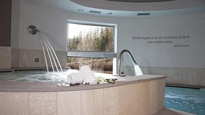 Ein Wellnessbereich mit Whirlpool, einem Fenster mit Blick auf Bäume und einem Zitat von Mahatma Gandhi an der Wand.