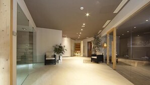 Eine großzügige Lobby mit modernem Design, inklusive Glastrennwand, einer Rezeption und einer Sitzecke mit Sesseln und Topfpflanzen.