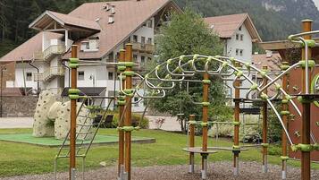 Children can play and climb on the playground equipment surrounded by a lush green field.