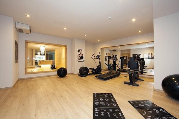 A modern gym with exercise equipment, a wooden floor, and a mirror reflecting the space.