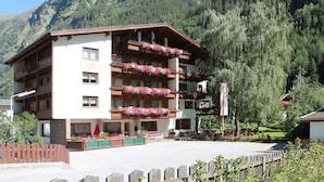 A multi-story hotel with balconies adorned with flowers, set against a mountainous backdrop.