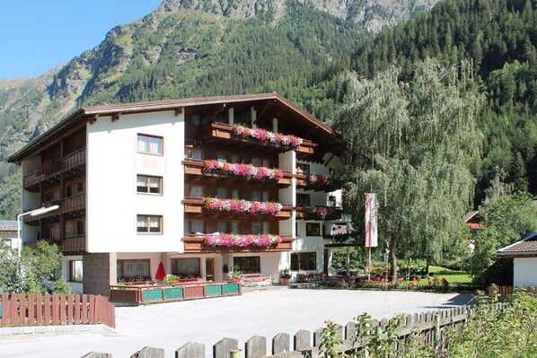 A multi-story hotel with balconies adorned with flowers, set against a mountainous backdrop. - Kaunertalerhof (FEICHTEN,KAUNERTAL)