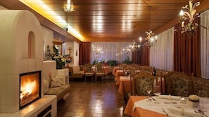A restaurant with a fireplace, wooden ceiling, and floral decorations. Tables are set with white tablecloths and silverware.