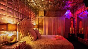 A luxurious bedroom with a tufted headboard, plush bedding, and ambient lighting. - Priamos - Adults Only (Athens)