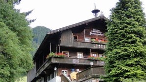 A traditional wooden building with multiple balconies, a staircase leading to the entrance, and a sign indicating it is a Pension Gasthof. - Fertinghof (OBERAU)