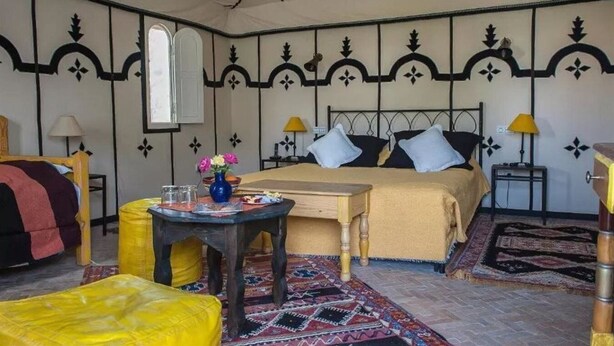A bedroom with a bed, two bedside lamps, a small table with a vase, and a patterned rug. - Dar Zitoune (Taroudant)