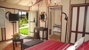 A bedroom with a large bed, a television, a small table with a vase, and a view of a garden through an open door. - Dar Zitoune (Taroudant)