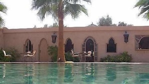 A pool with clear water, surrounded by a building with arched windows and a palm tree. - Dar Zitoune (Taroudant)