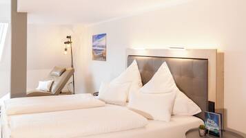 Une chambre d’hôtel avec un grand lit, un fauteuil massant, une petite table avec une plante et un luminaire fixé au mur.