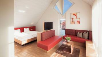 A modern room with a bed, a red sofa, a TV, and a view of a building through a window.