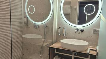 A modern bathroom with a glass-enclosed shower, a wooden vanity with a white sink, and two illuminated mirrors.