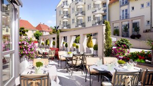 An outdoor café with tables and chairs, surrounded by buildings and greenery. - Traube am See (Friedrichshafen)