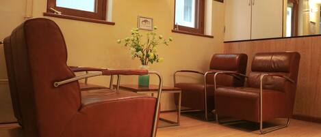 A room with a brown leather chair, a small table with a vase, and a clock on the wall.
