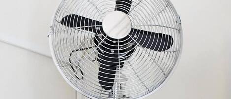 A standing electric fan with a protective grill and three blades, mounted on a metal stand.