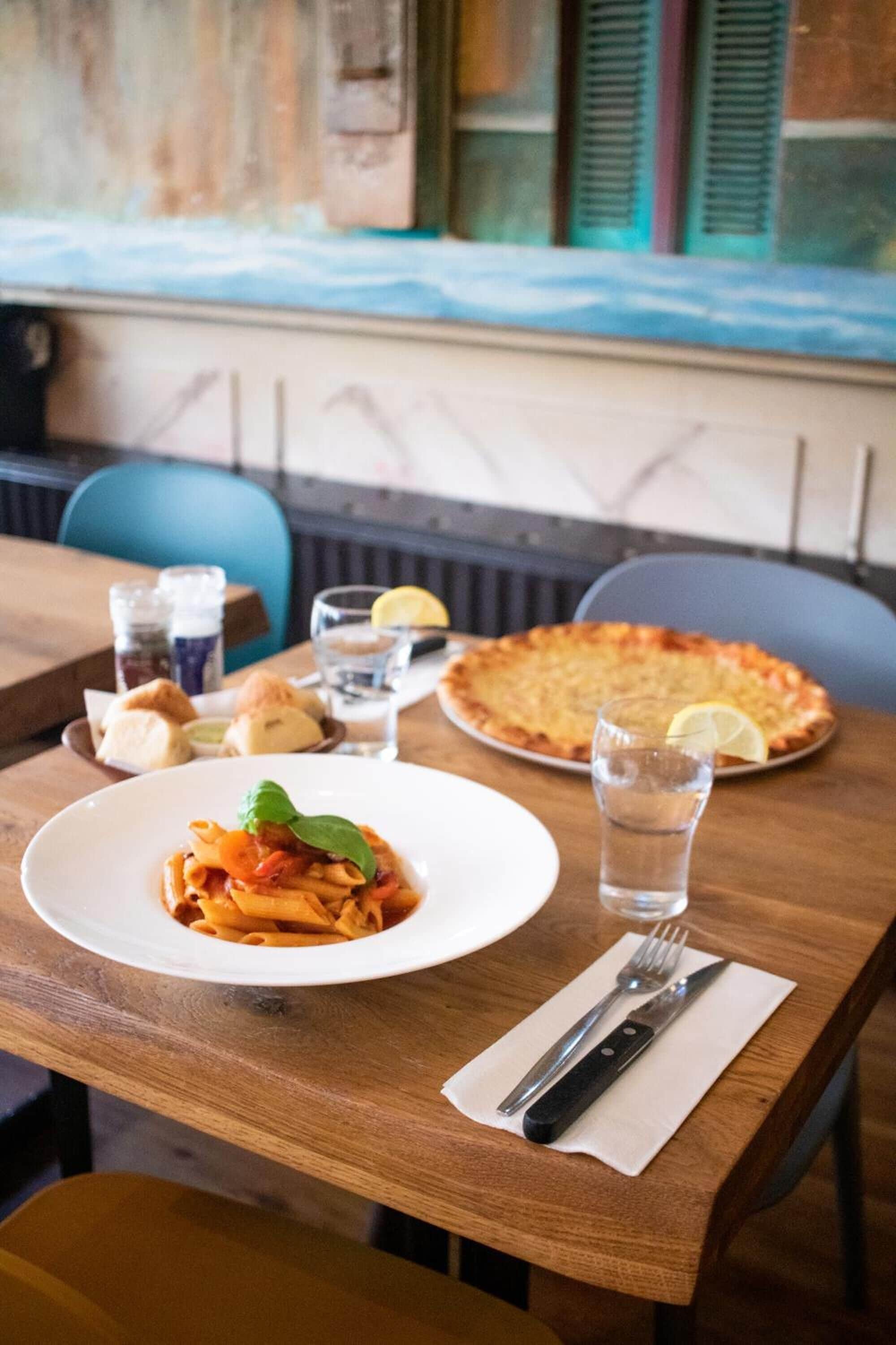 Ein Esstisch mit einer Pasta-Käseplatte, einer Pizza, einem Glas Wasser und einem Zitronenschnitz.