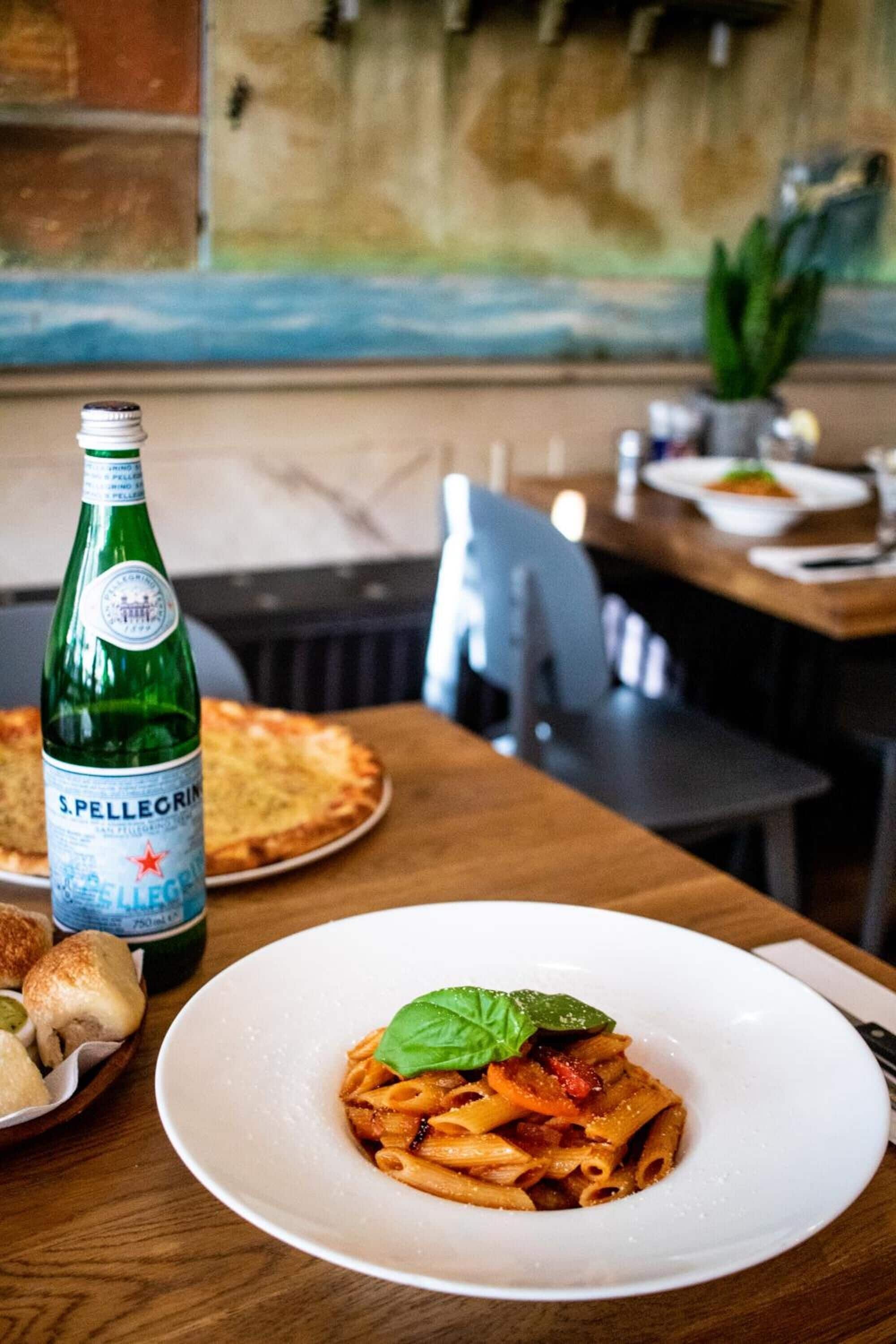 A dining table with a plate of pasta and a bottle of Pellegrino water.