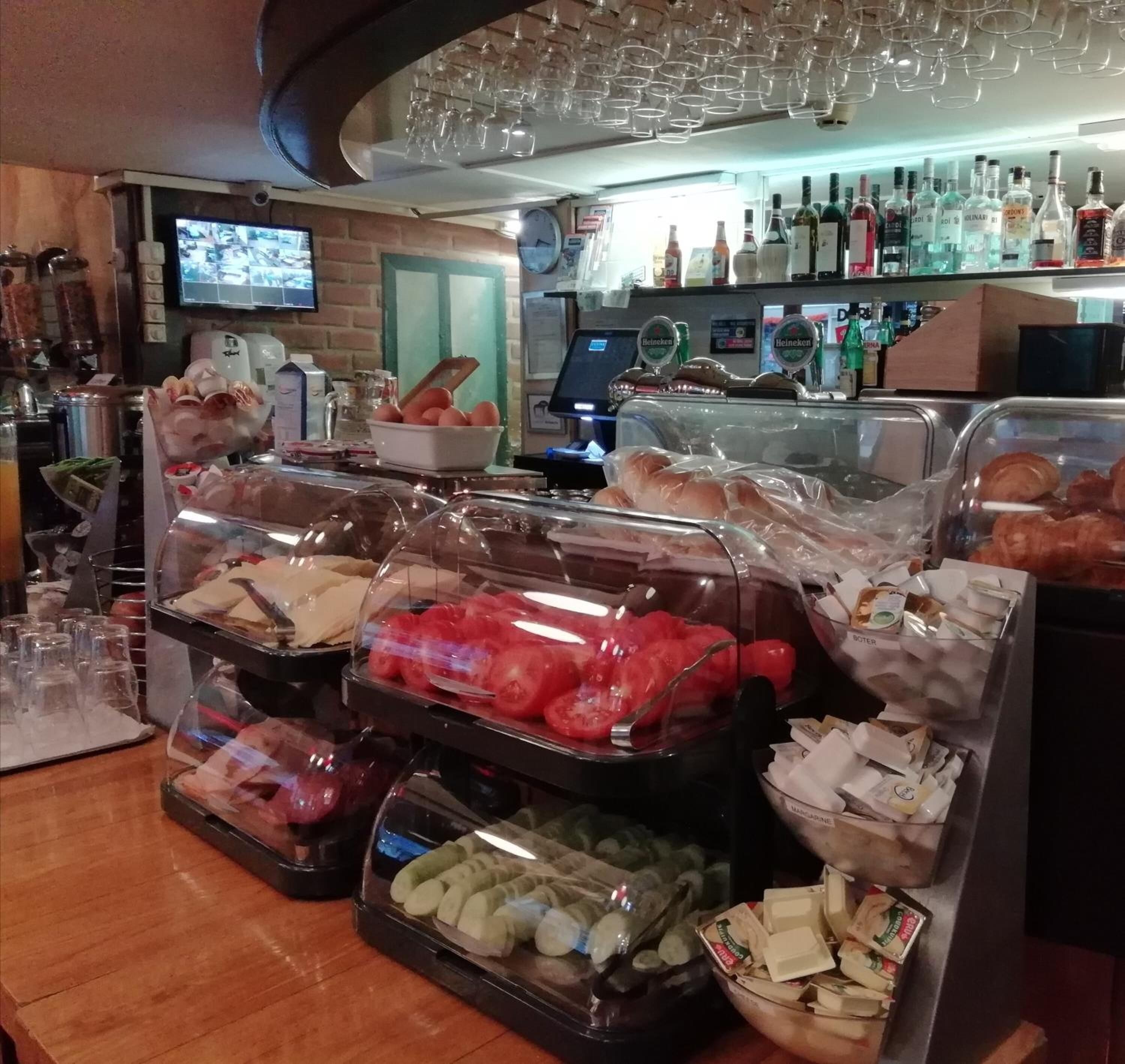 A buffet area with various food items, including bread, tomatoes, and cheese, and a bar area with bottles and glasses.