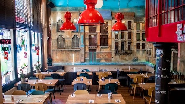 A restaurant with wooden tables and chairs, red pendant lights, and a mural on the wall. - Hotel Doria (Amsterdam)